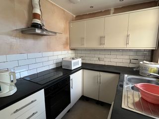 A small U-shaped kitchen during the renovation stages. Plaster walls, exposed extractor fan, cream mounted cabinets, black countertops and white subway tiles on the walls