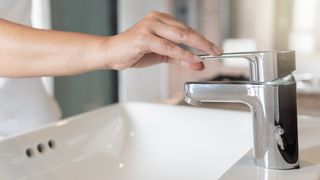 A close up of a woman turning on a water faucet in a home