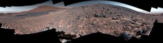 a panoramic view of the surface of Mars from the top of a ridge, littered with rocks and hills