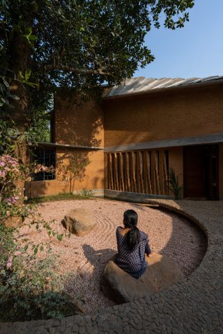 Woman sitting in round courtyard outside architectural house in India, designed by Wallmakers