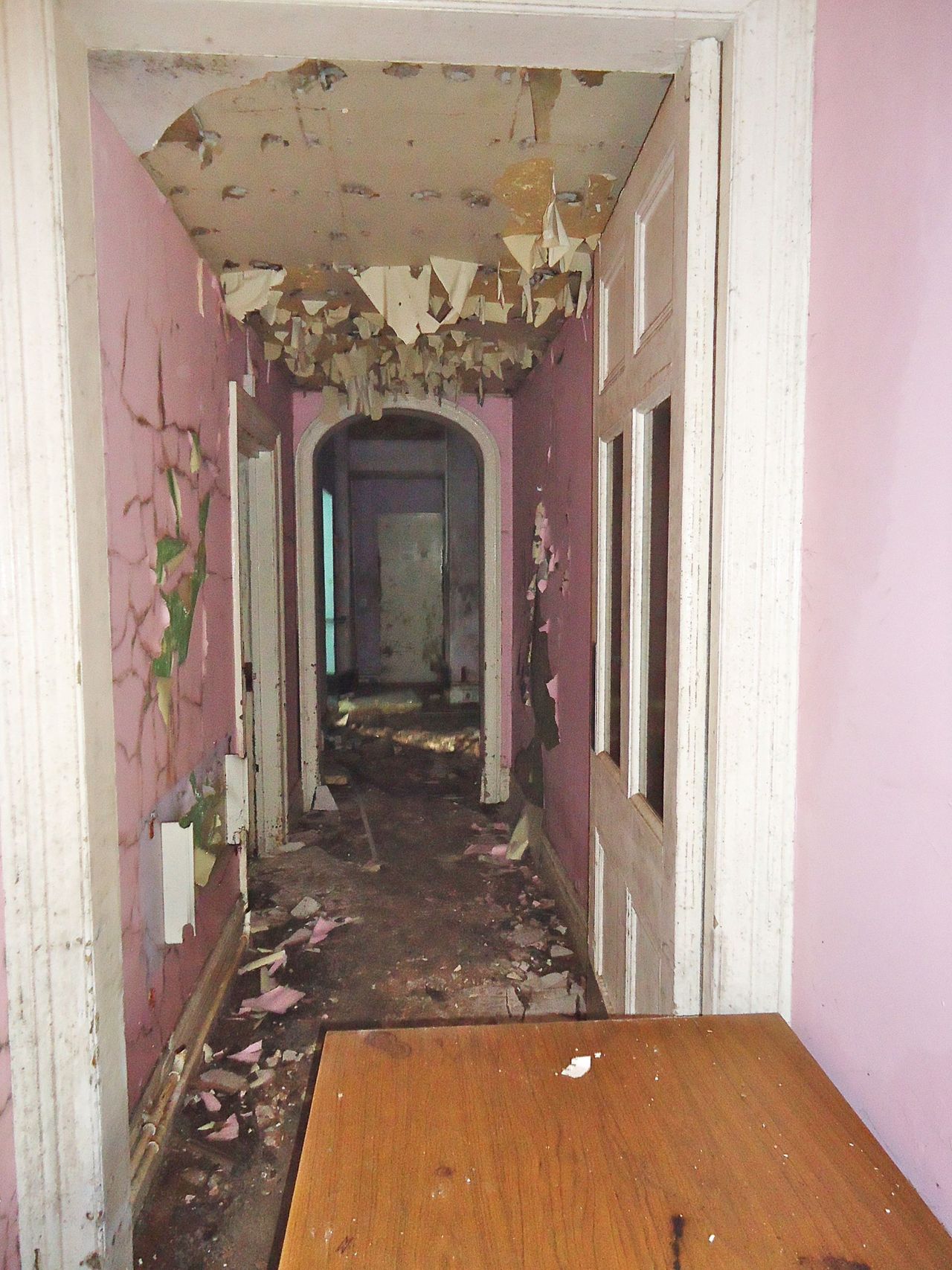 Before picture of an arched hallway with pink paint peeling off the walls