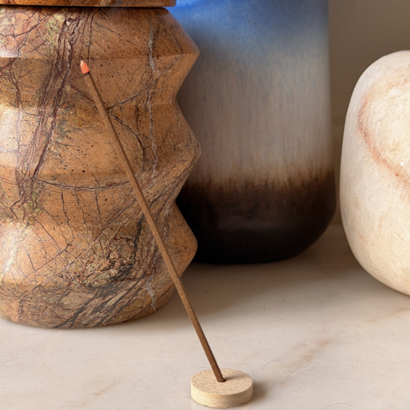 A photo of an incense stick in an incense holder on a table with vases