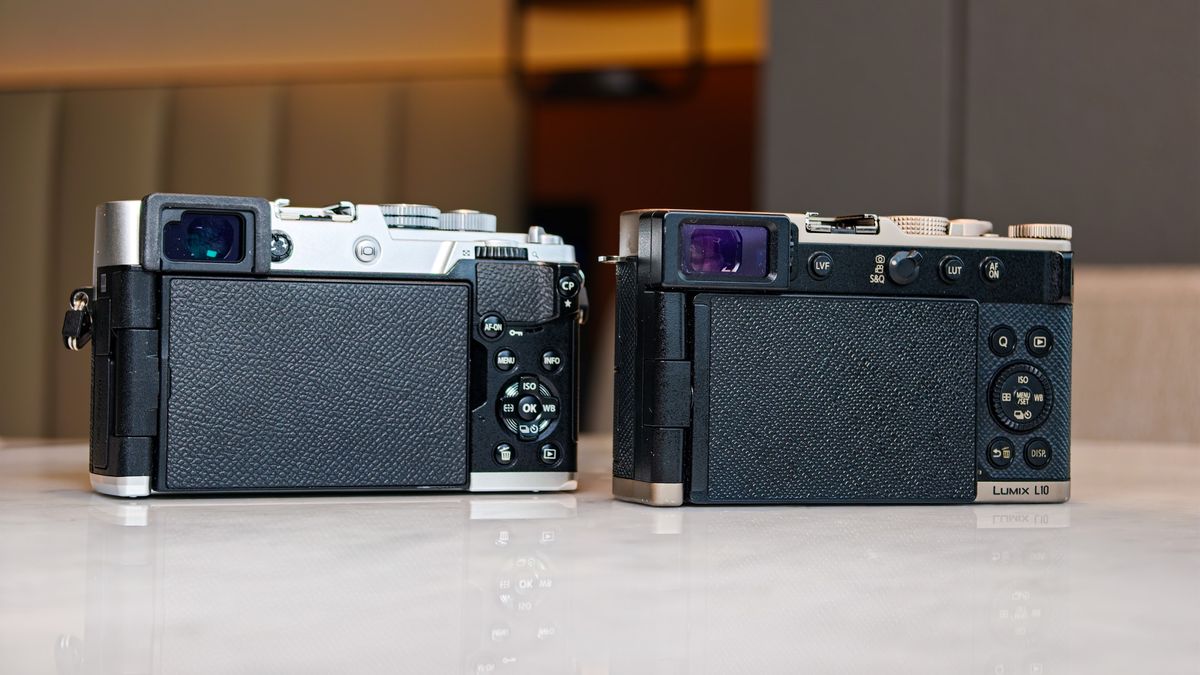 OM System PEN vs Panasonic Lumix L10: two micro four thirds cameras side by side on a white marble surface with lamp light in the background