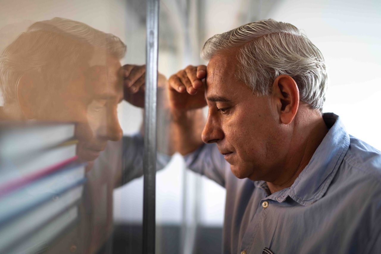 A man leans his head into his reflection with an upset look on his face.