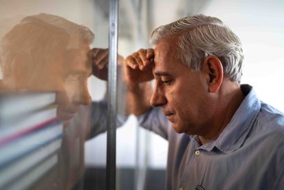 A man leans his head into his reflection with an upset look on his face.