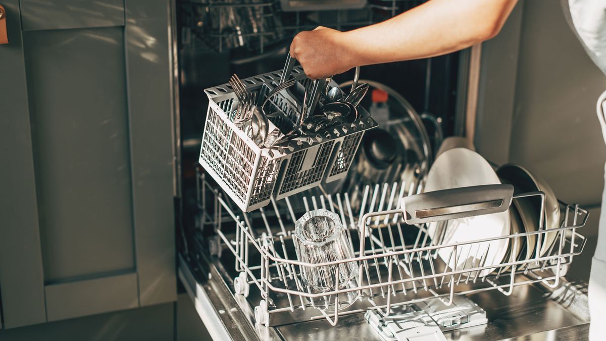 Person putting cutlery into integrated dishwasher with grey kitchen cabinet doors in background