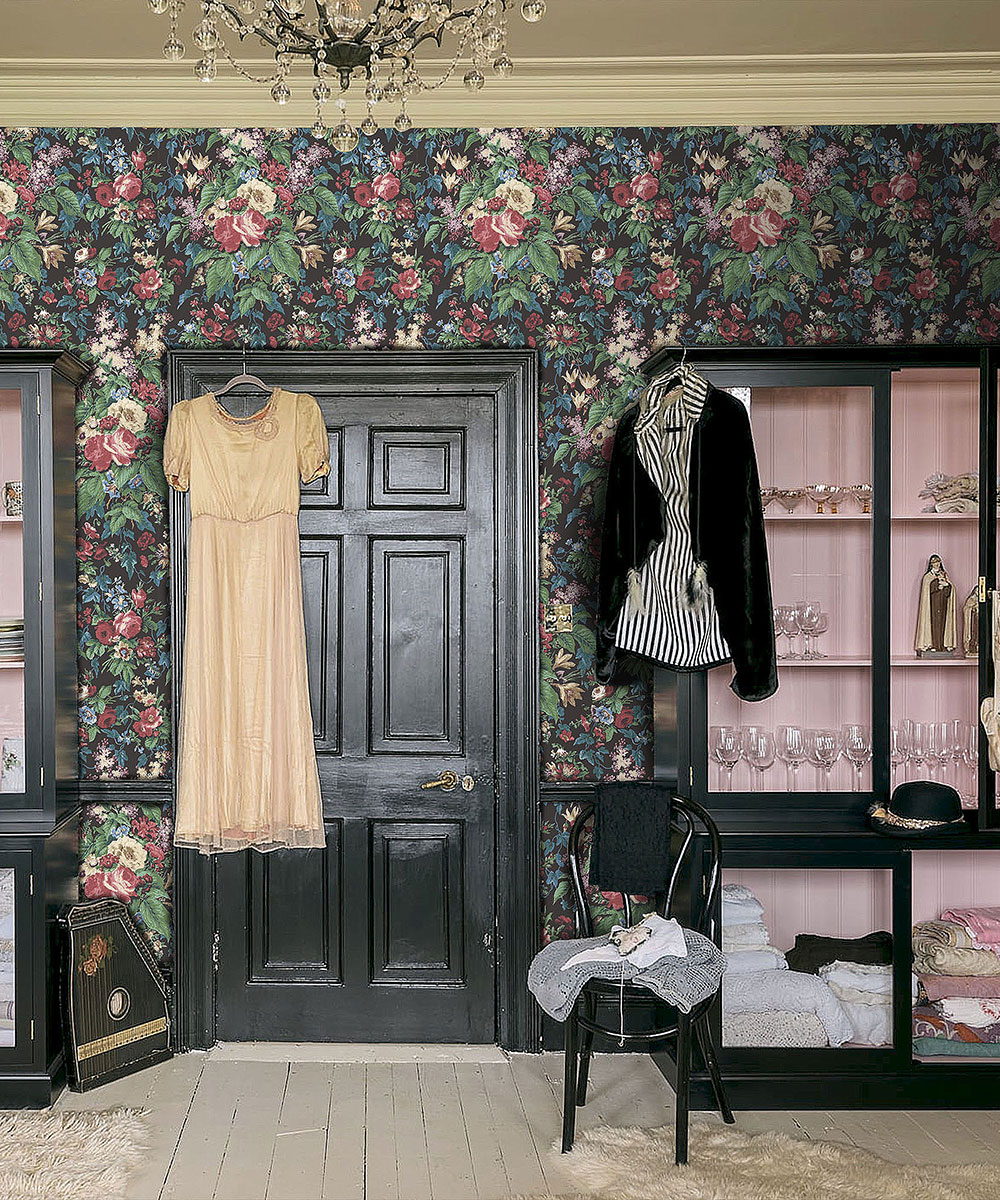 Dark floral wallpaper surrounding a black door with a dress hanging up