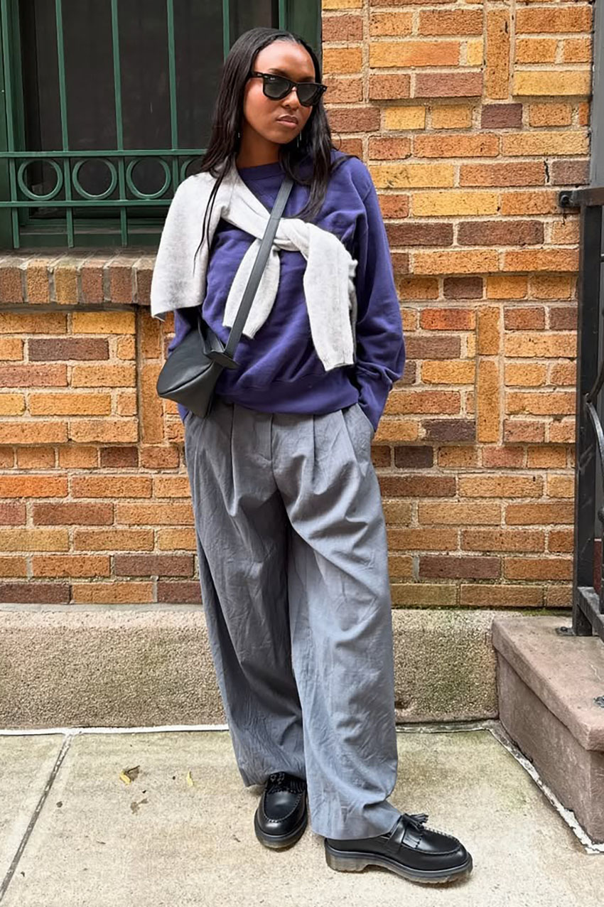 A woman wearing a purple longsleeve, gray pants, and black loafers