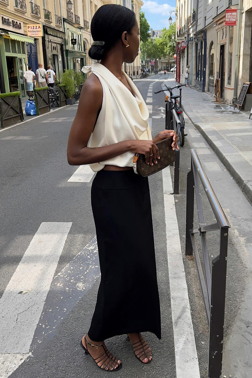 best strappy sandals shown in a photo of a French woman standing in the street wearing a white silk top with a black maxi pencil skirt and black strappy heel sandals and a brown clutch bag