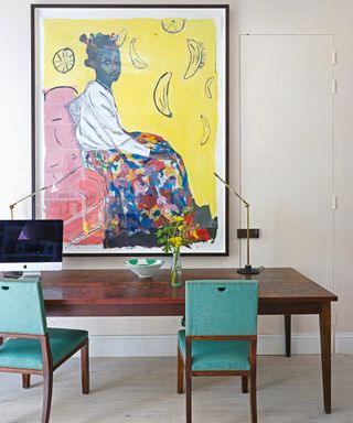 office with statement painting, wooden table and green chairs