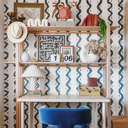 Home office desk setup, patterned wallpaper, velvet desk chair and decorated shelving