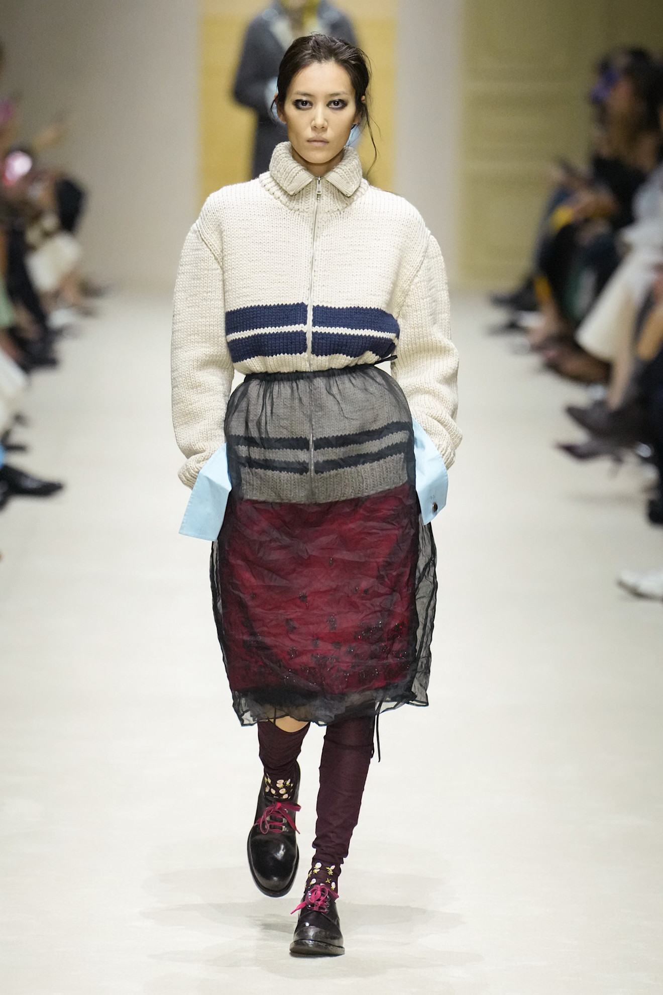 A model at the F/W 26 Prada show wearing a chunky knit sweater with a sheer pencil skirt.