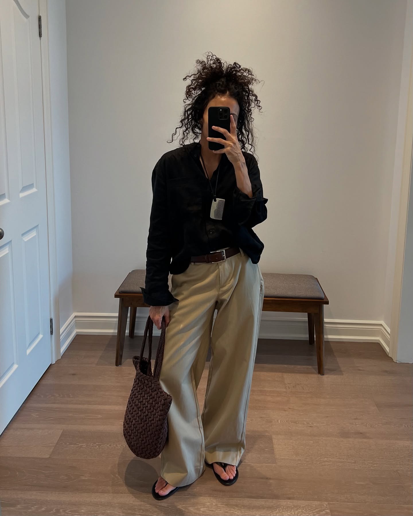 Neelam Ahooja wearing a black button-down shirt, The Row's comb necklace, Banana Republic khaki pants, and a bag by The Row.