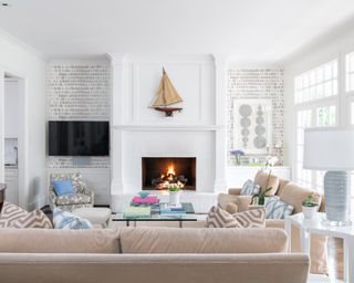 Neutral living room with view over back of sofa to second sofa, coffee table, armchair, and lit fireplace with gray patterned wallpaper in alcoves at either side