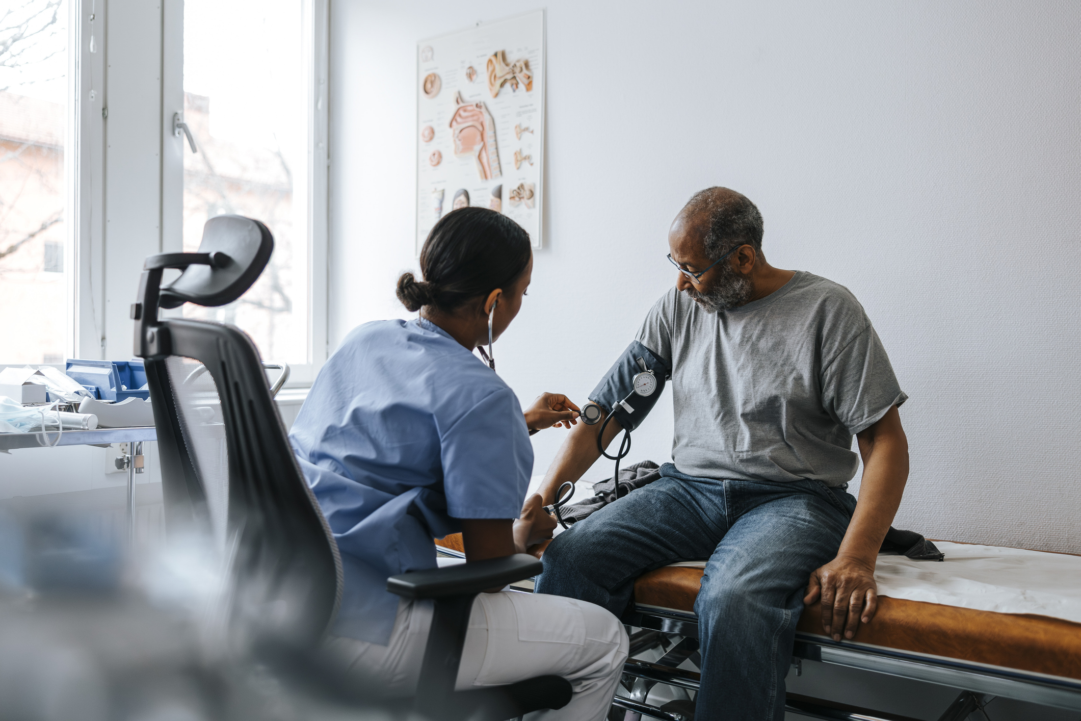 Female doctor checking senior patient&#039;s blood pressure sitting on bed in examination room at hospital