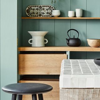 Picture of a green, Japanese inspired kitchen with open wooden shelving and black stool.