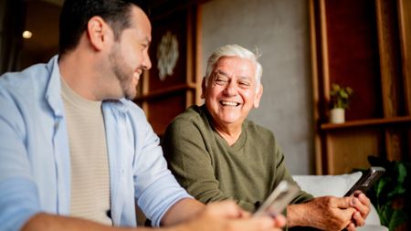 Father and adult son talking while using mobile phone at home 
