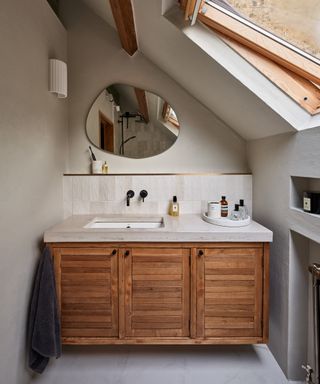 loft conversion bathroom with wooden vanity, large countertop with inset sink, wooden skylight and recesses cut into wall to house radiator and shelf space