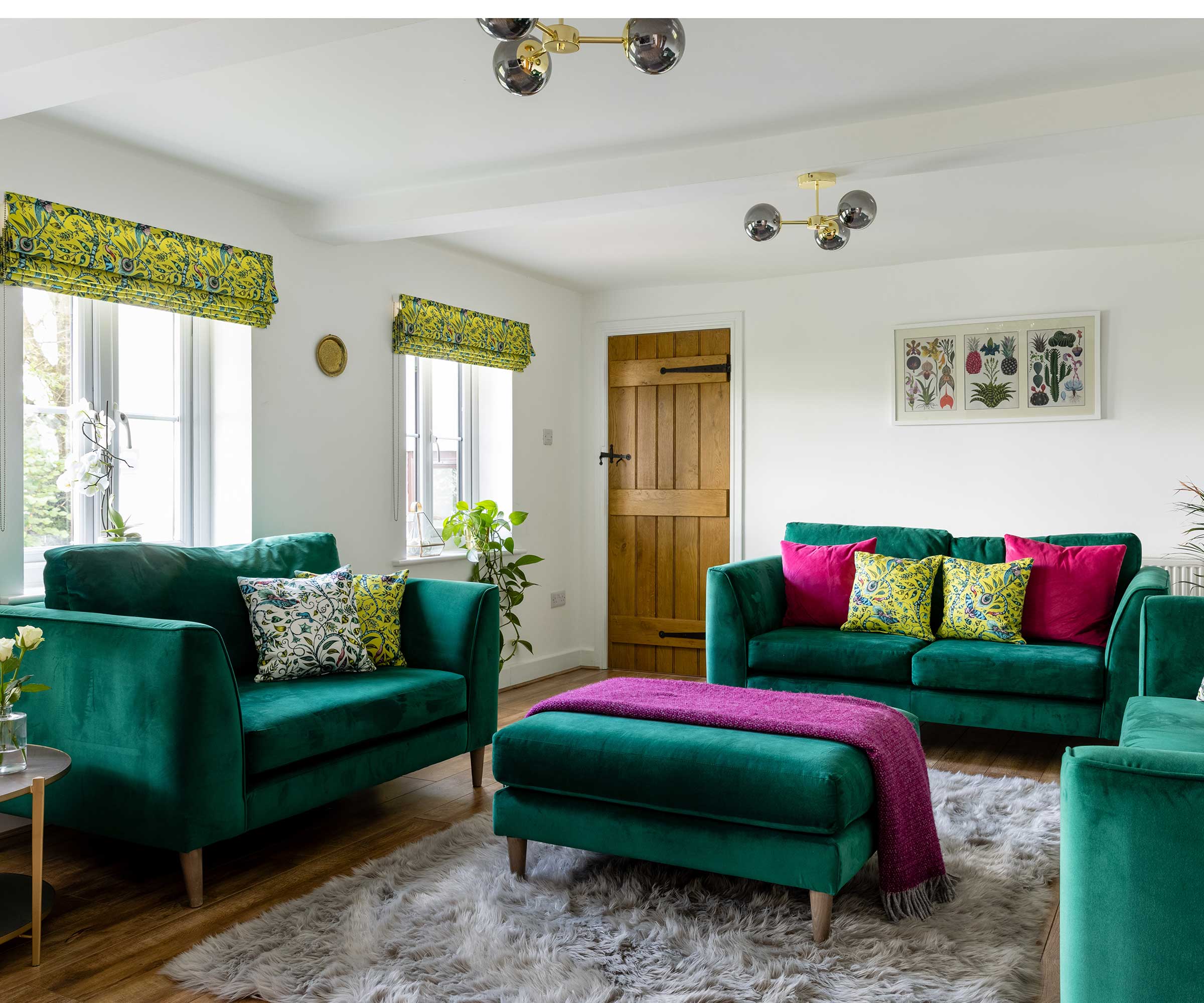 living room in a cottage with green velvet sofas and a grey rug on wooden flooring