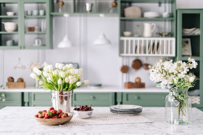 A kitchen with two vases of flower on a marble island