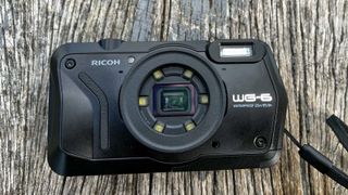 Black Ricoh WG-6 waterproof camera on a weathered plank of wood