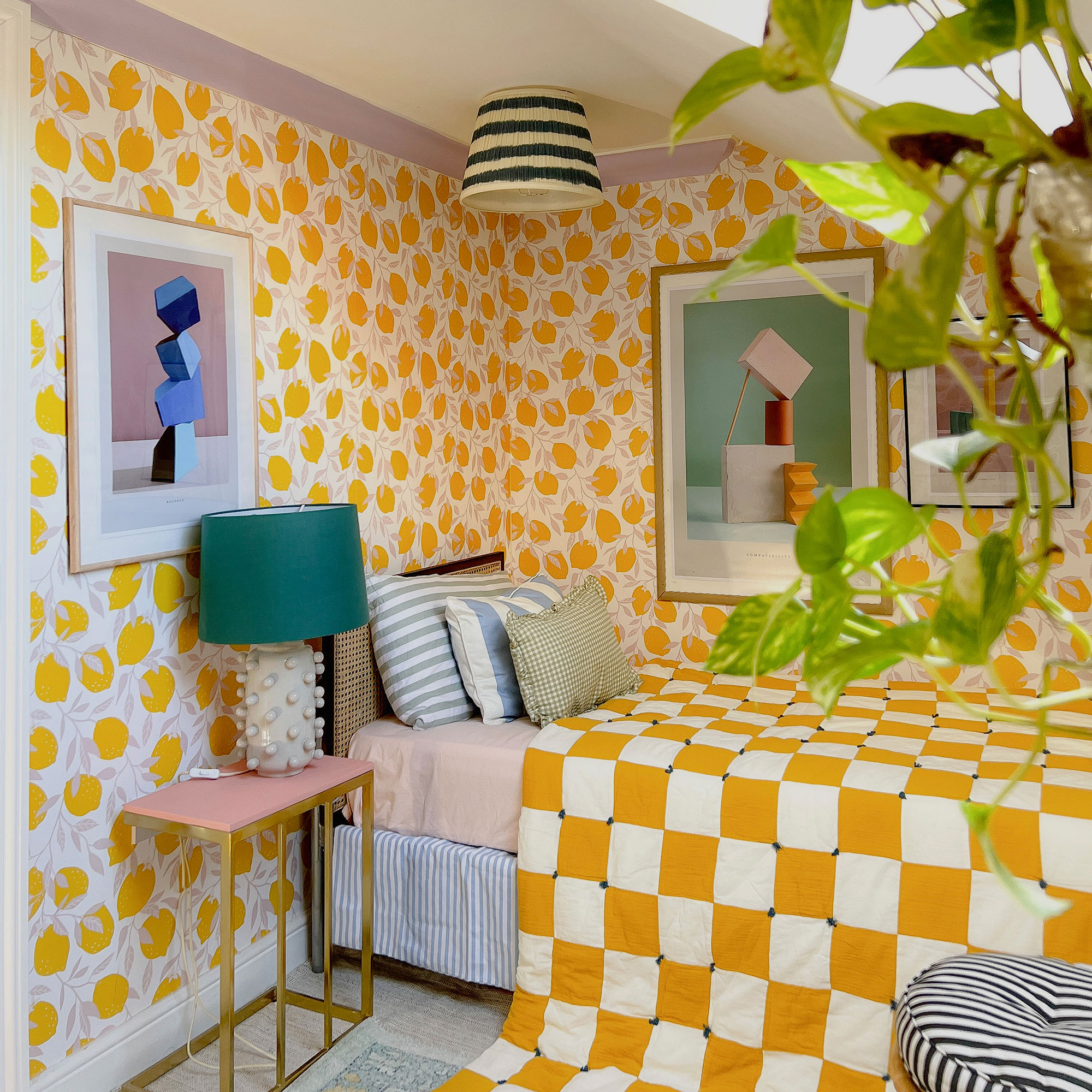 Bedroom with yellow and white patterned walls, graphic artwork, yellow and white checked bedspread, pink and bronze bedside table and oversized ceramic table lamp