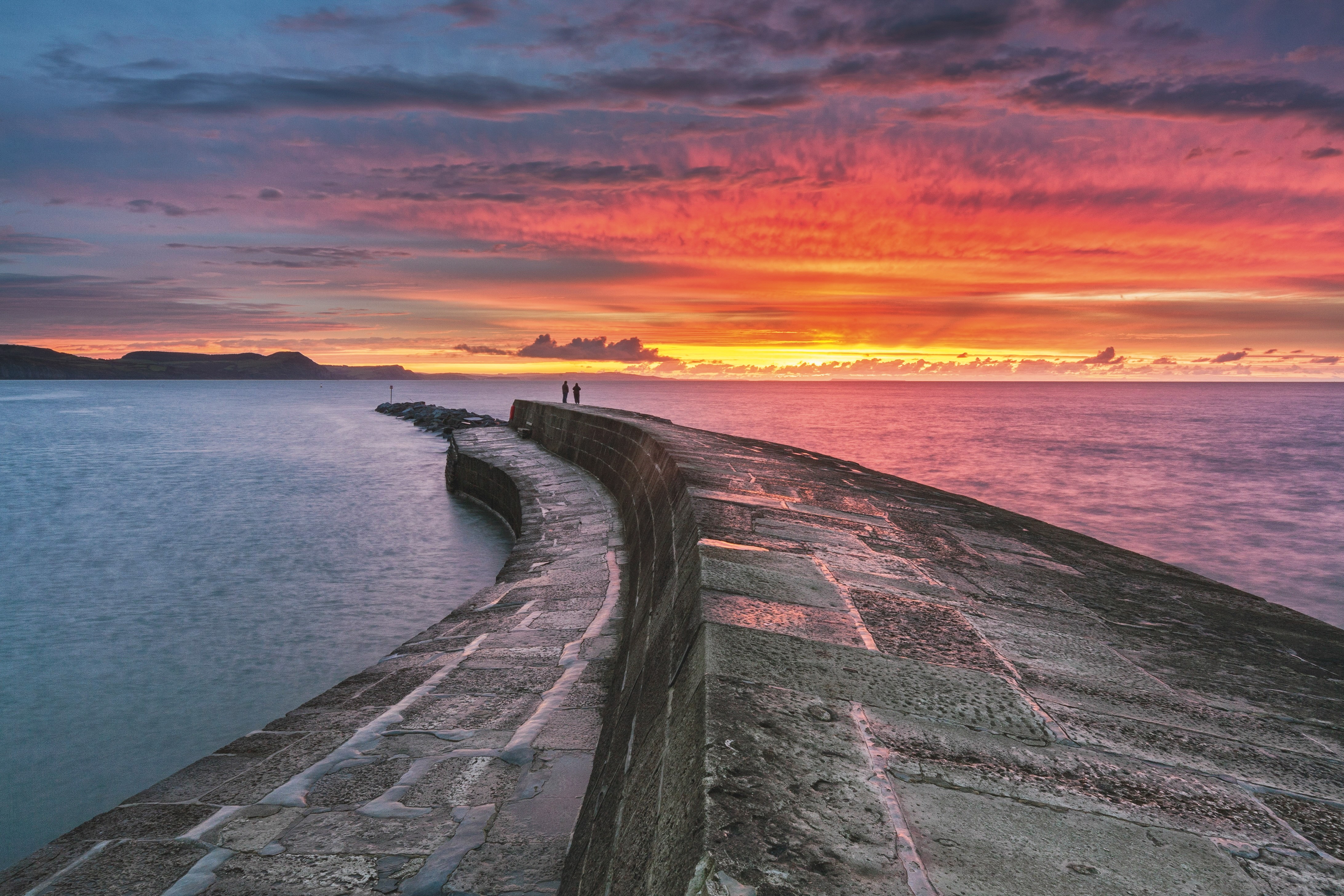 Couple standing on The Cobb at sunrise, Lyme Regis, Dorset, England
