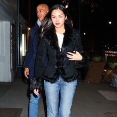 Olivia Rodrigo wears blue cigarette jeans with square-toe boots and a fur-trimmed jacket.