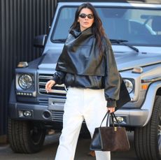 Kendall Jenner in a black leather bomber jacket, white pants, and bag, by Phoebe Philo