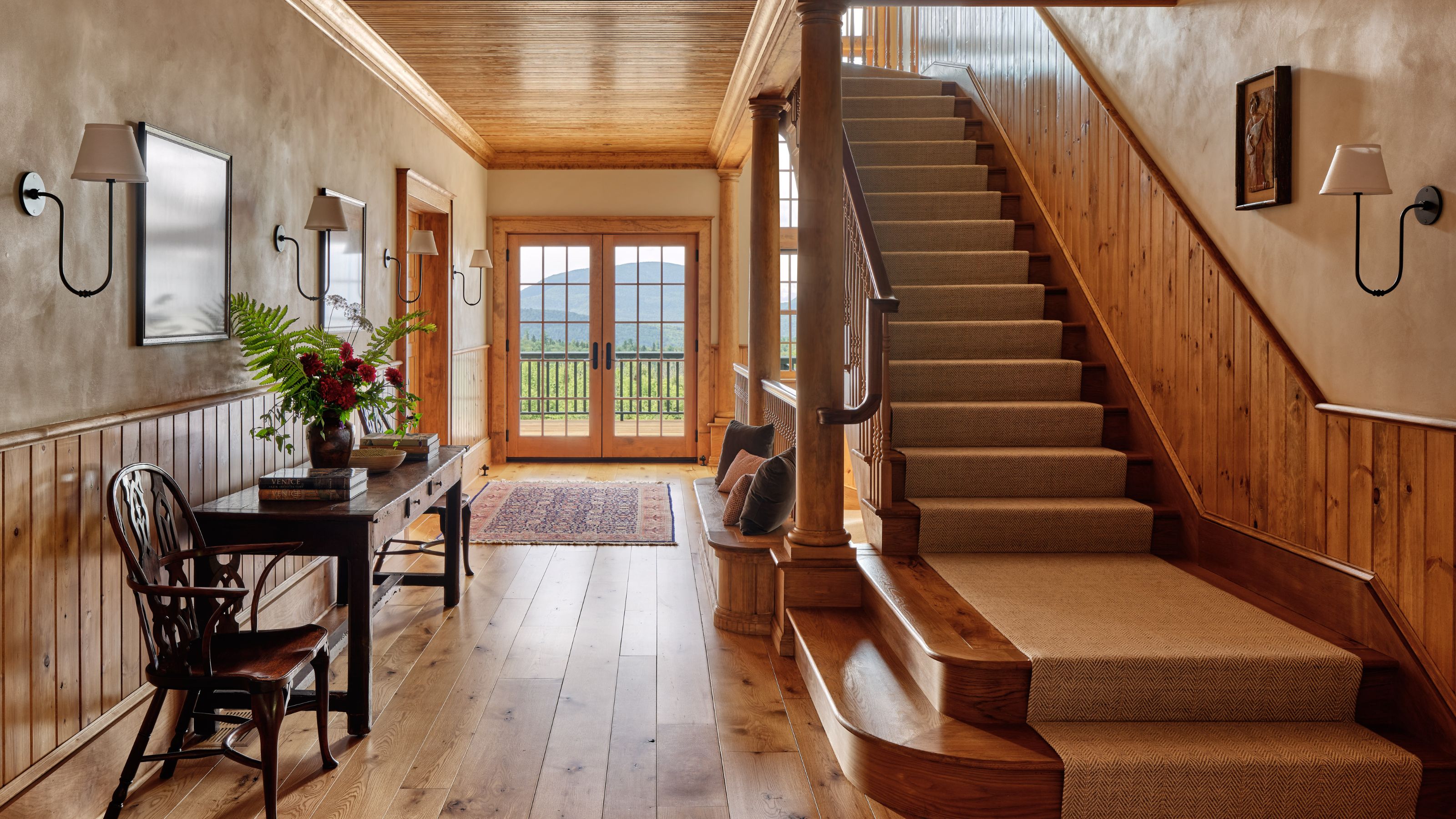 a large hallway with wide plank wooden floors, wood panelled walls at half height, a panelled ceiling and a large wooden staircase