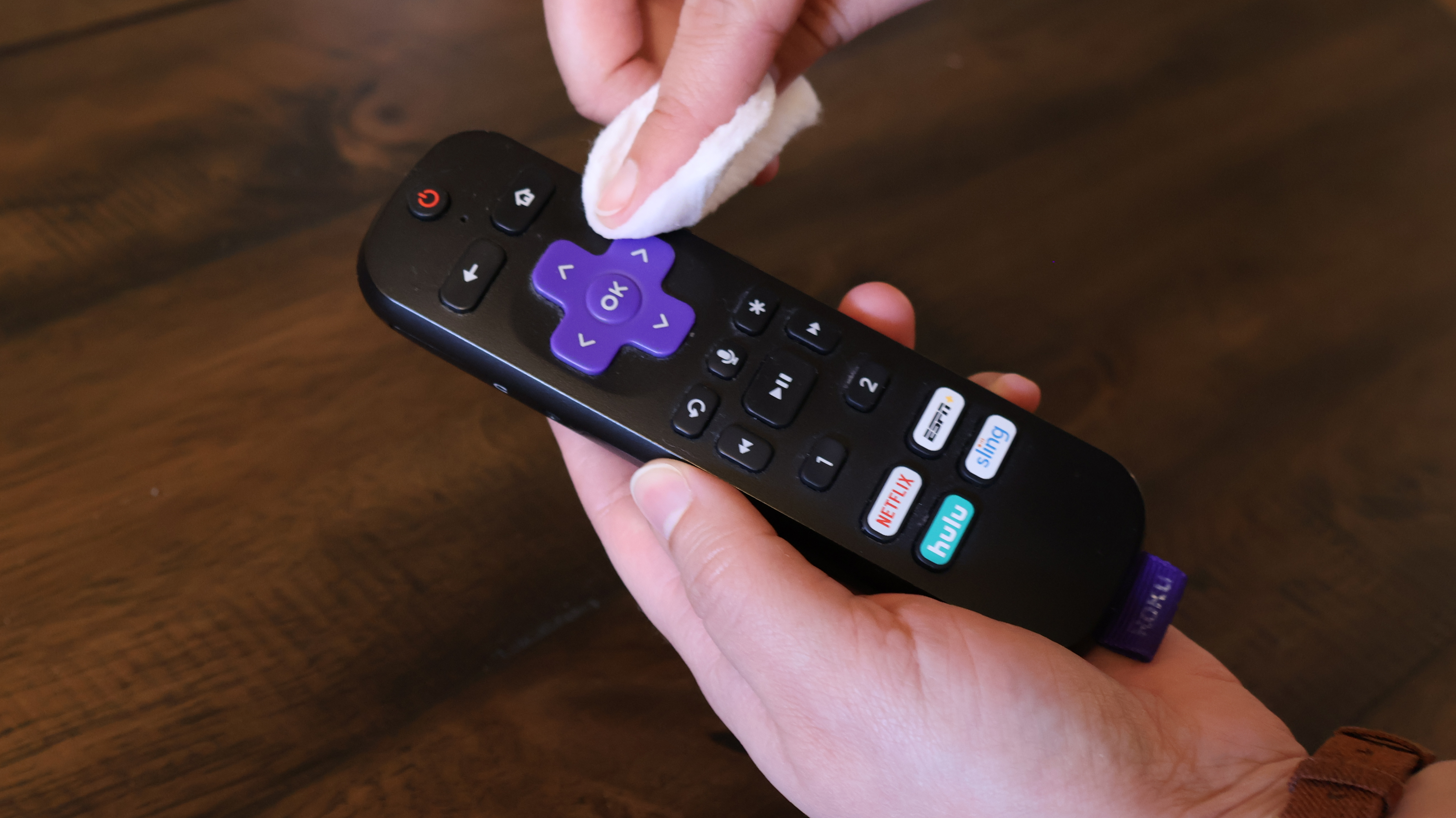 A pair of hands sanitizing a Roku-branded TV remote control with a dampened cotton round