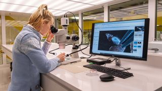 A researcher works at a microscope with a monitor hooked up to it