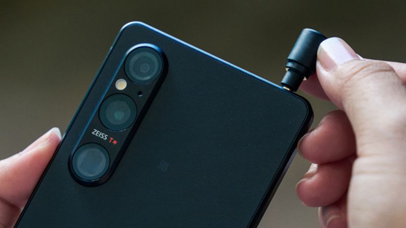 A hand pushing a headphone jack into a Sony Xperia 1 V phone