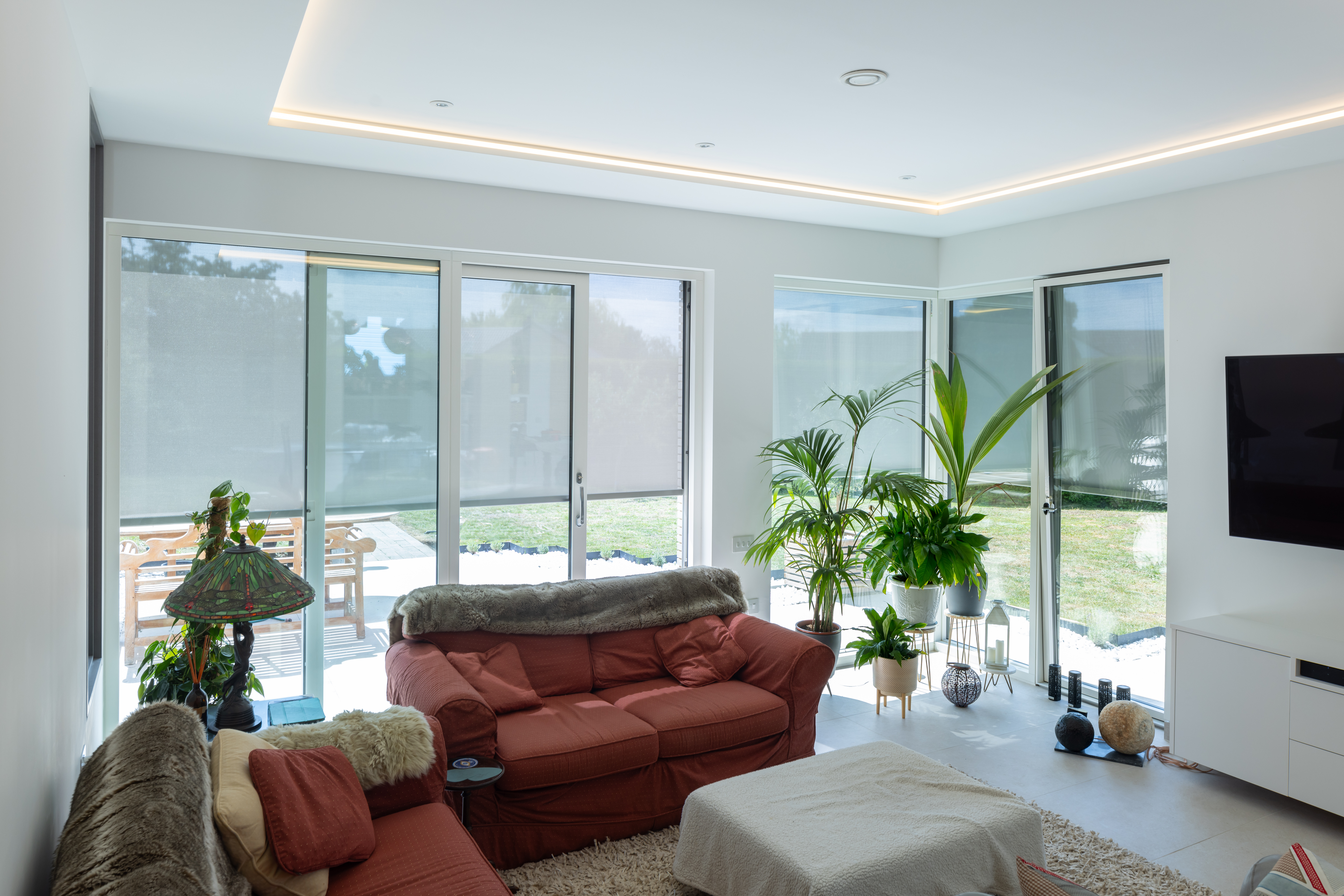 Contemporary living space with orange furniture, white walls, plants and floor to ceiling windows covered with Kensington Blinds external shading