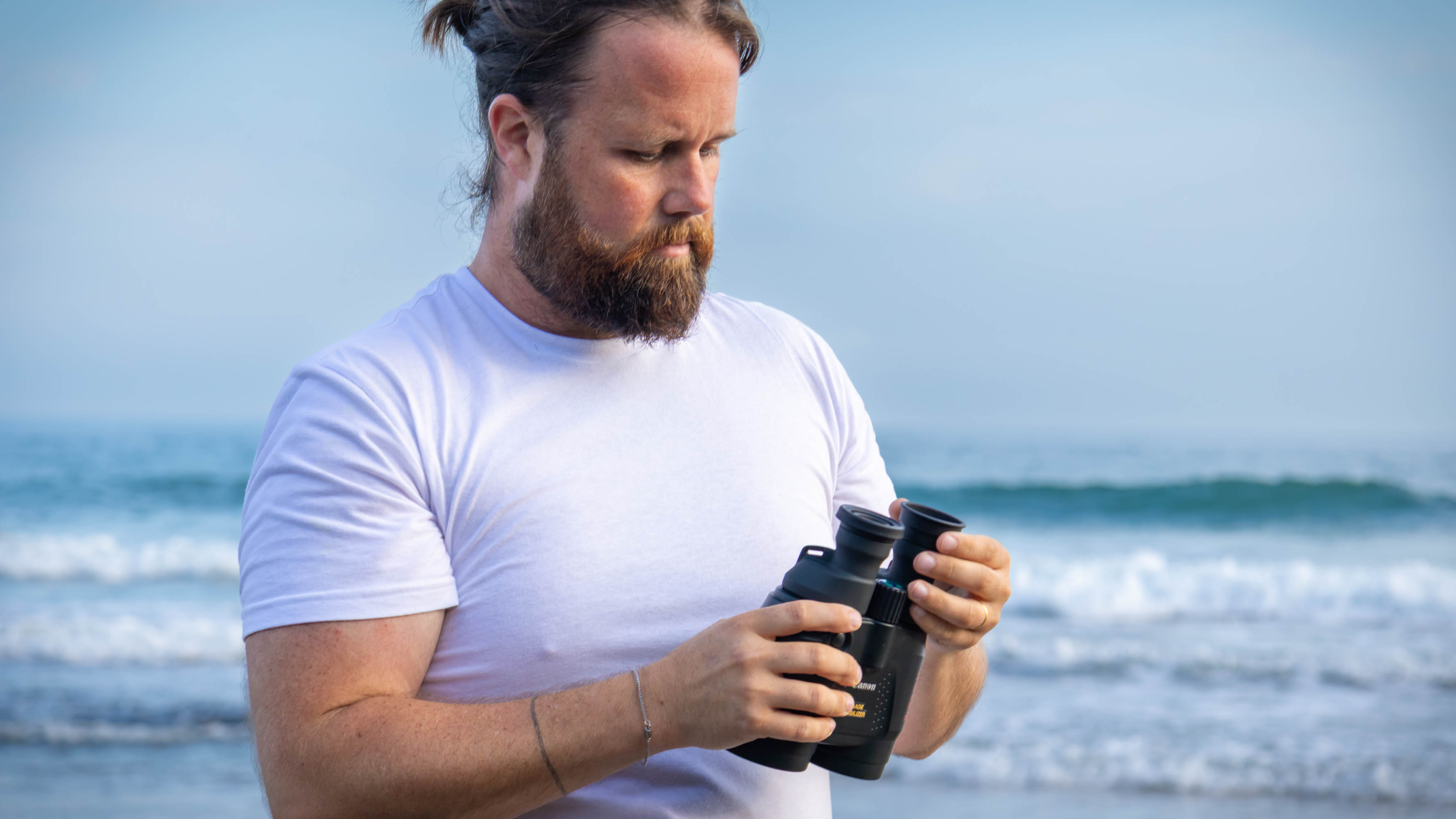 A male by the sea holding the Canon 18x50 IS binoculars, adjusting the eyecups.