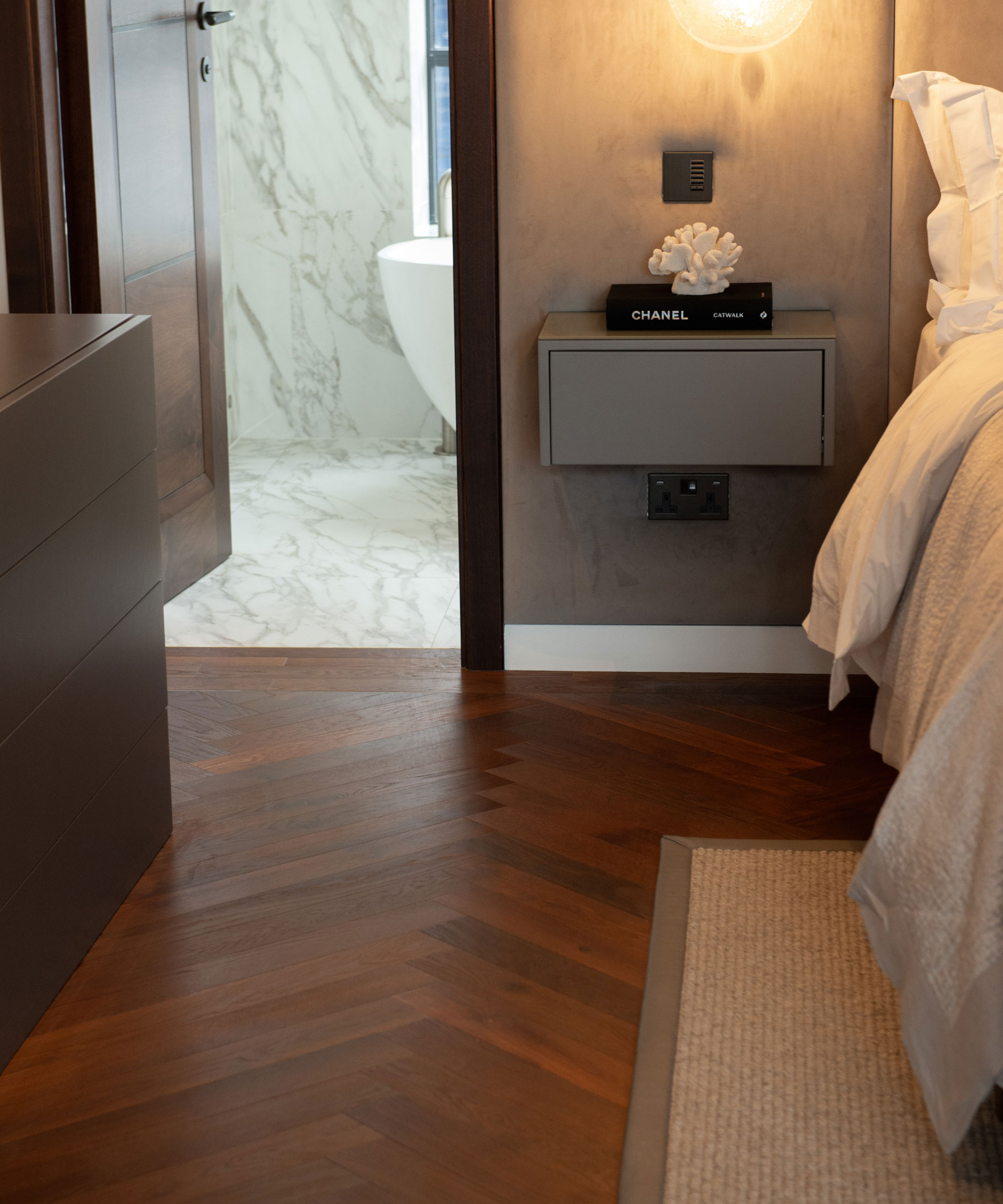 Bedroom with dark herringbone engineered flooring leading to en suite