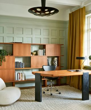 office with wooden fitted shelves accent chair and green paneled walls