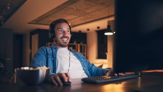 Happy attractive freelancer sitting at his desk, staring at monitor, playing computer game at night