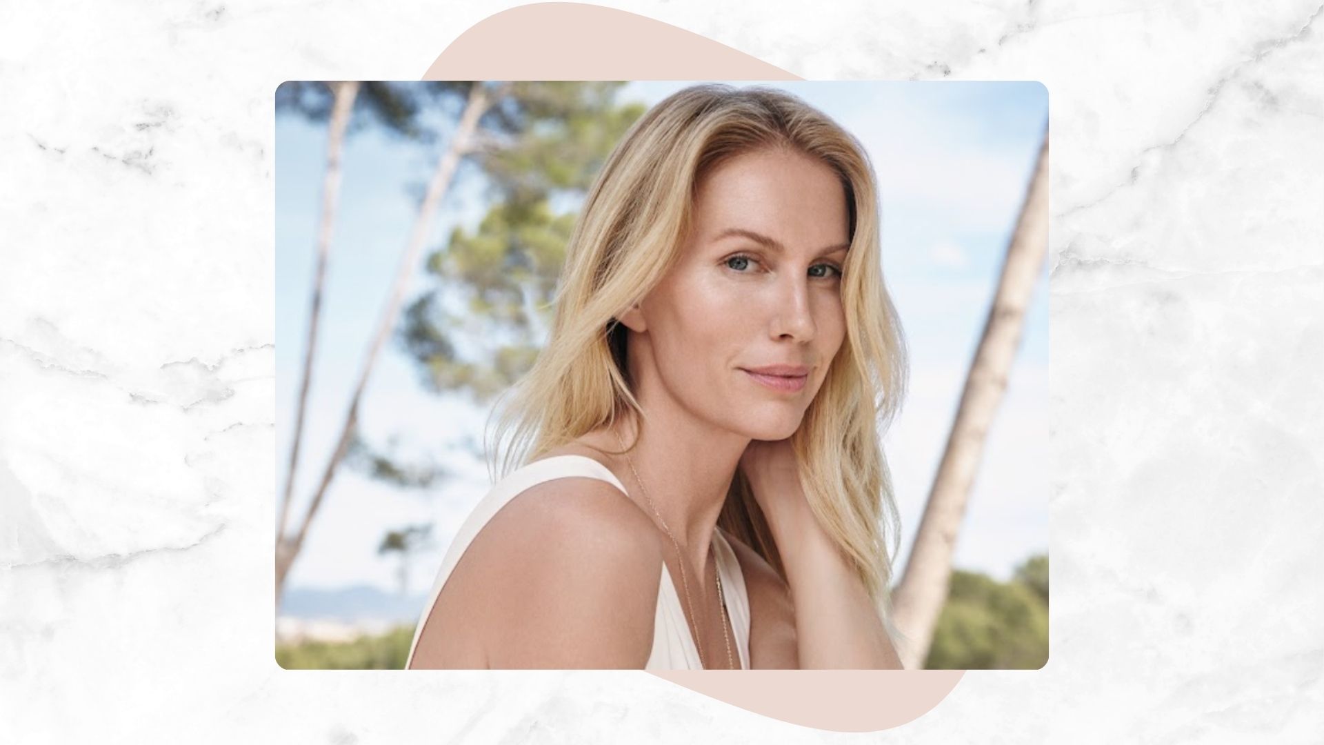 marble backdrop with an image of a blonde woman, with smooth skin, wearing a white dress with a blue sky and trees behind her