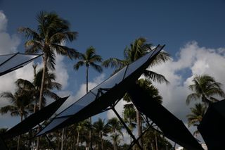 Daytime image, close up of silver solar reflectors, cloudy blue sky, palm trees