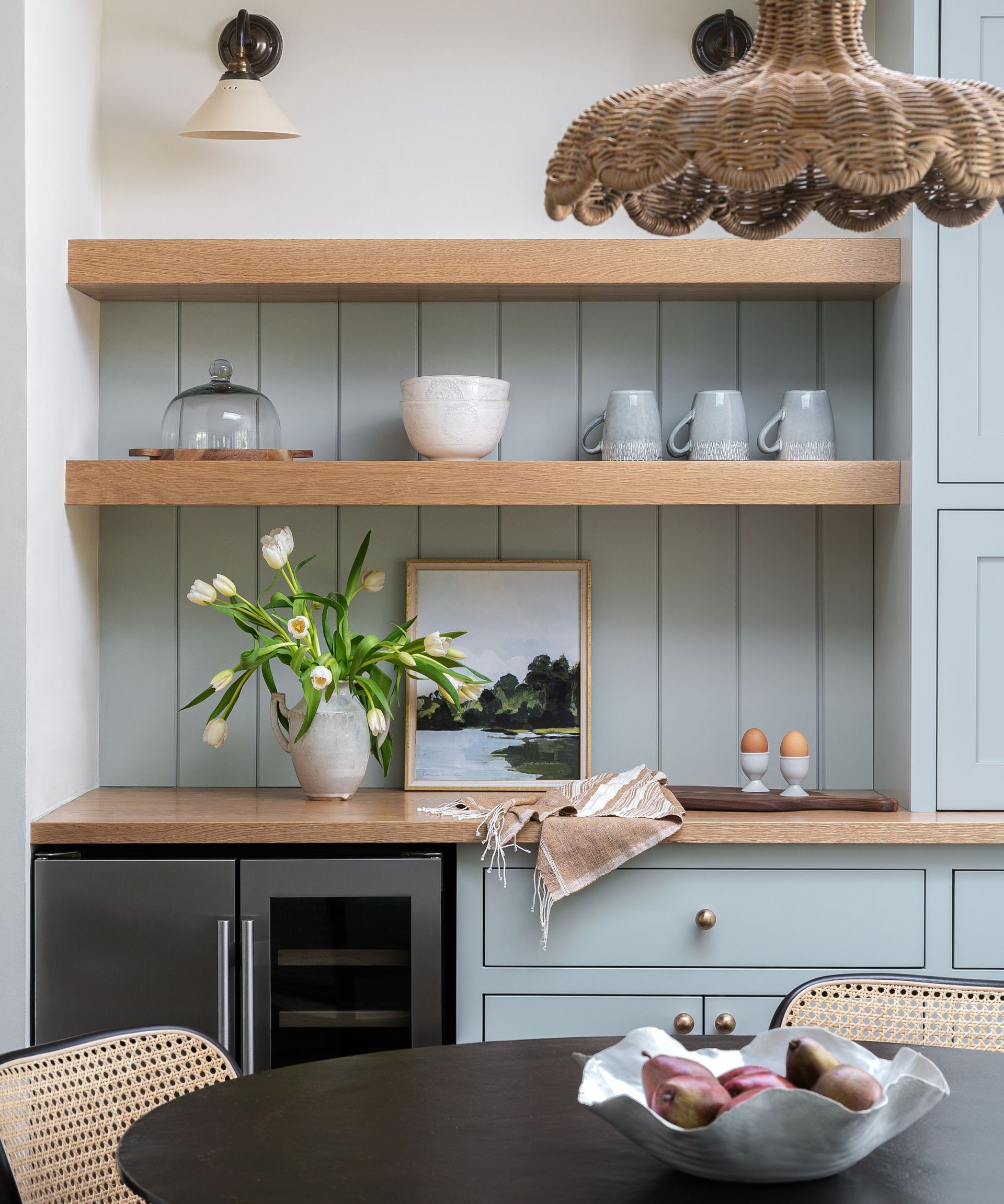 A coffee bar with light blue cabinets and paneling, wooden shelves, and black round table, and wicker accessories