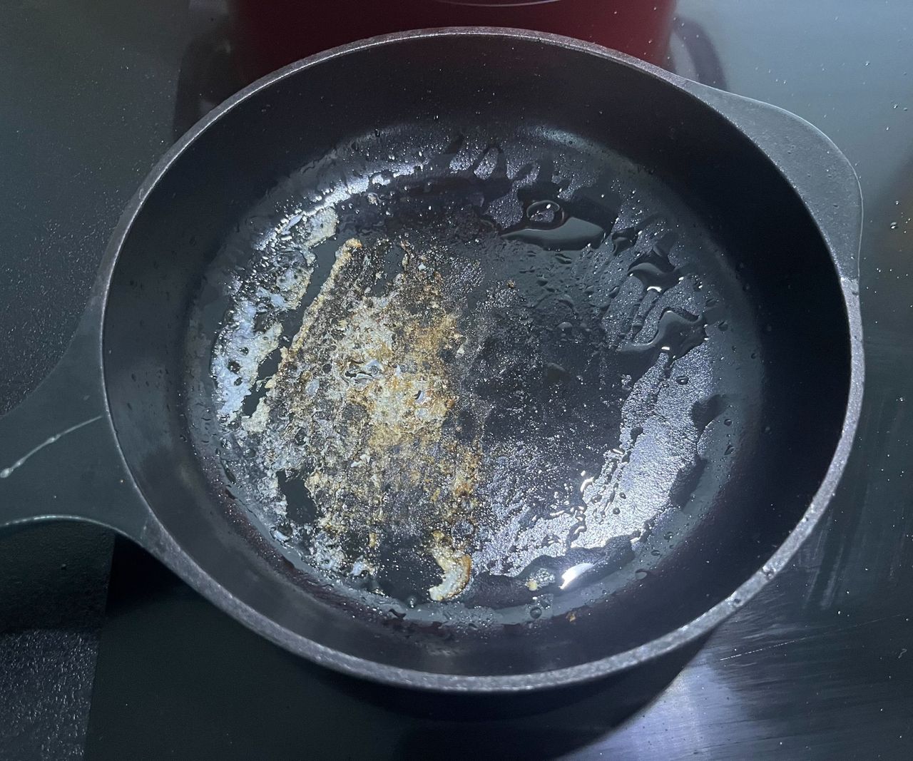 A back cast iron skillet with stuck on egg in the base.