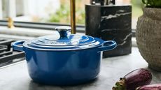 A dark blue Le Creuset Dutch oven on a marble kitchen counter