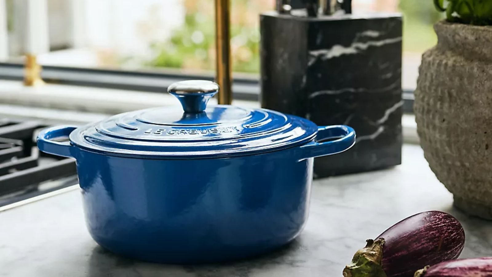 A dark blue Le Creuset Dutch oven on a marble kitchen counter