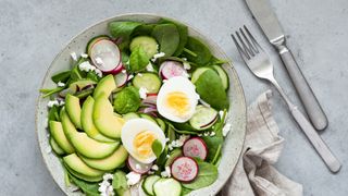 A bowl of sliced avocados, eggs and leafy greens