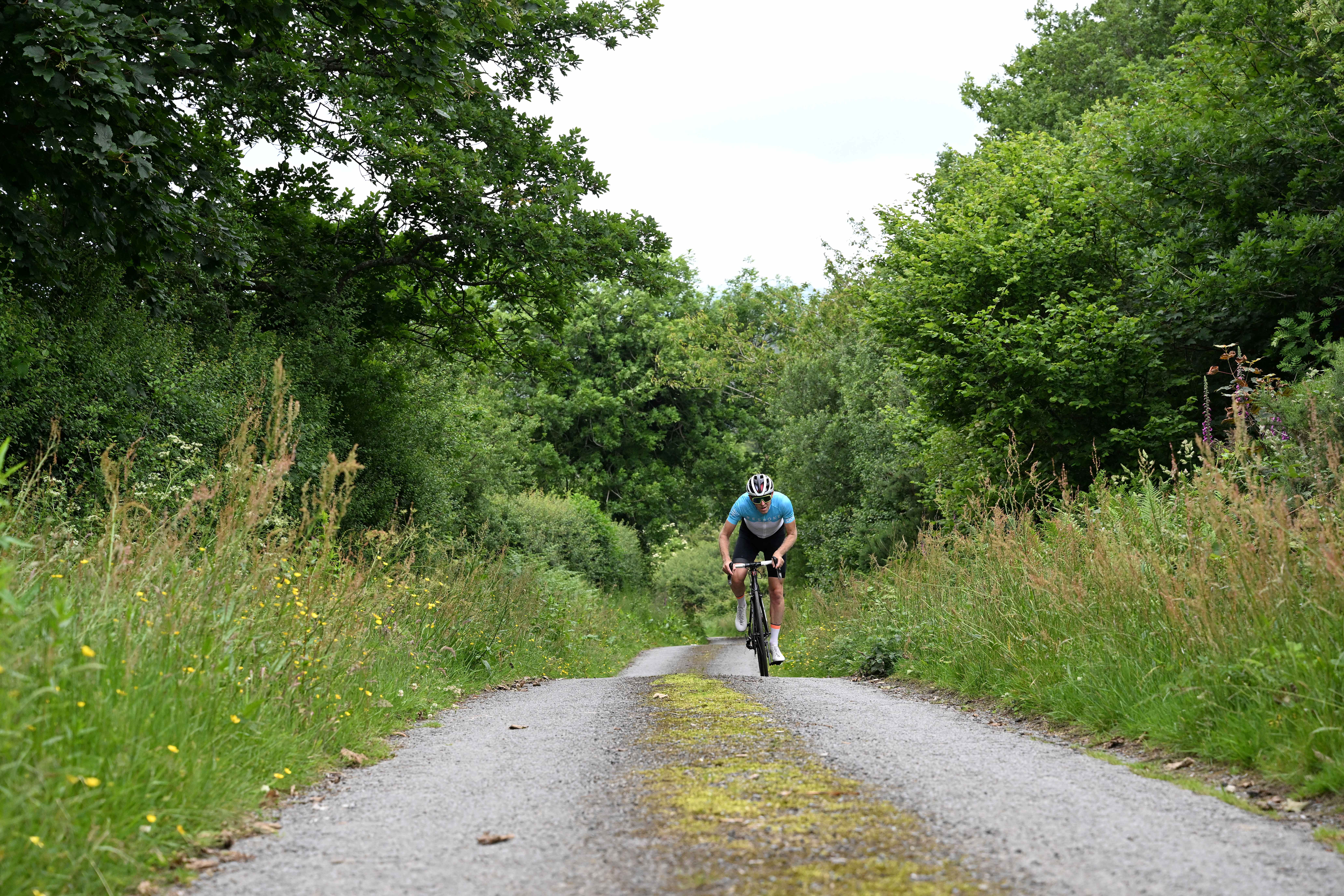 man cycles up country lane hill