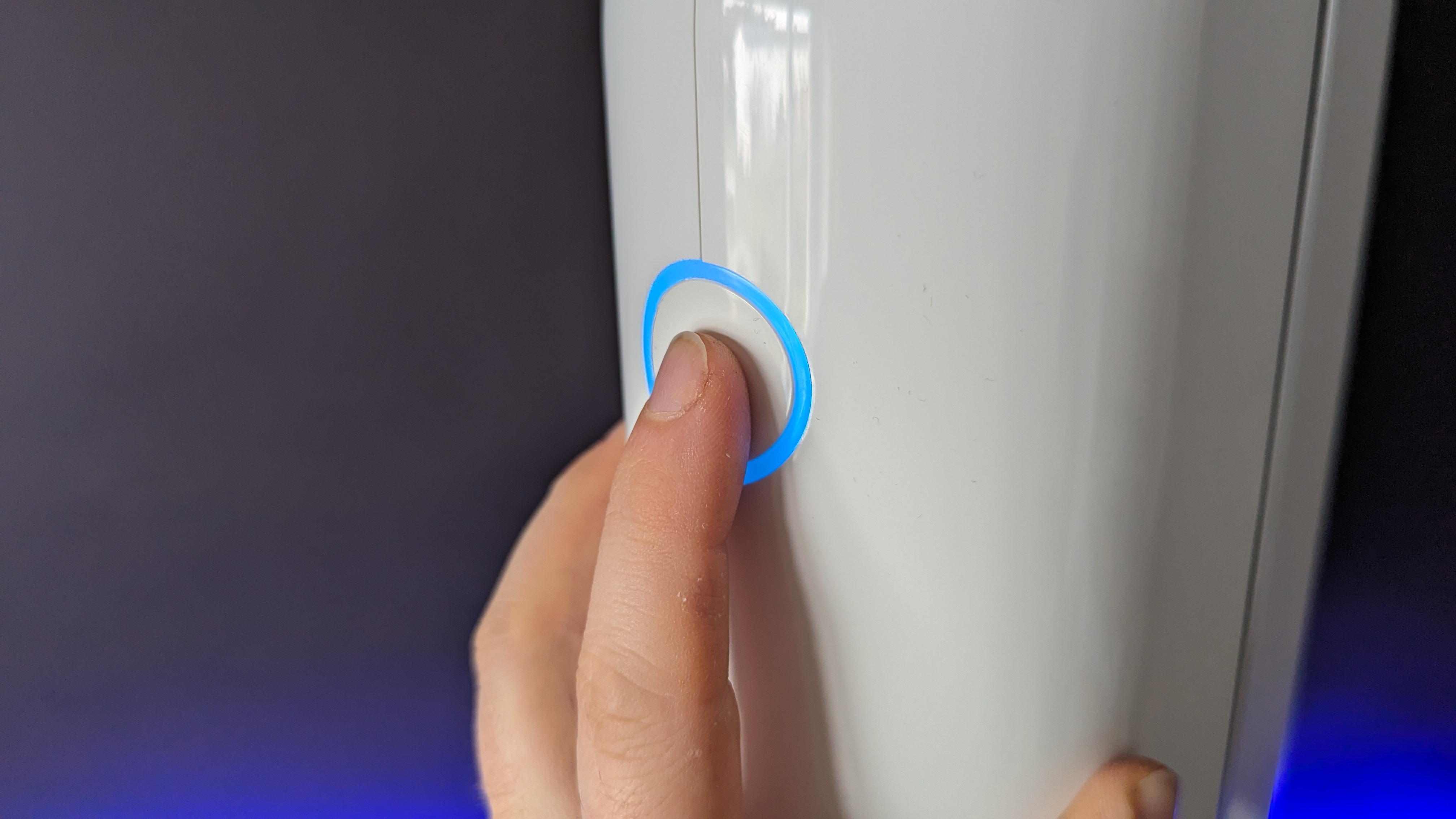 Vaonis Vespera II being switched on by the author's finger, a white button glows blue,in front of a black background with a blue light shining