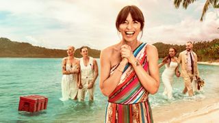 Davina standing hands clasped together, big smile, with two couples standing in the ocean behind her. Red crate also in the picture.