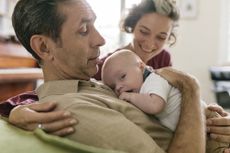 Close-up of proud grandparents embracing newborn. Couple is sitting on livingroom couch.
