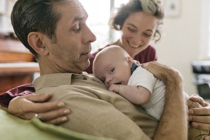Close-up of proud grandparents embracing newborn. Couple is sitting on livingroom couch.